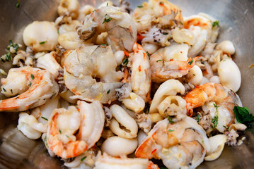 Mixed Seafood Ready for Cooking with Herbs. A bowl of mixed raw seafood including shrimp and squid, seasoned with herbs, prepared for a delicious meal.