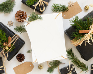 Envelope and card near Christmas decor, gift boxes and green fir branches  top view, mockup