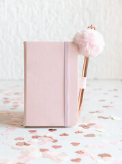 Pink hardcover notebook with fur pen  near hearts on white table close up, textbook mockup