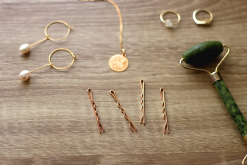 Pearl headband and barrette, golden eyeglasses, gold necklace, earrings and rings, jade face roller and hair pins on wooden background. Various elegant gold accessories. Selective focus.