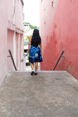 Young beautiful black-haired woman from the back walking in an alley of red colored walls.