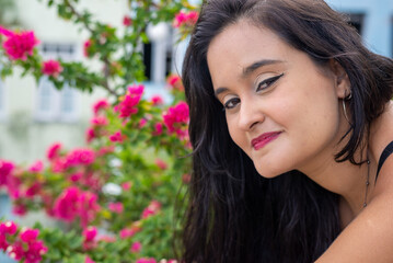 Naklejka premium Portrait of a beautiful young woman, with long black hair, looking at the camera with flowers in the background.