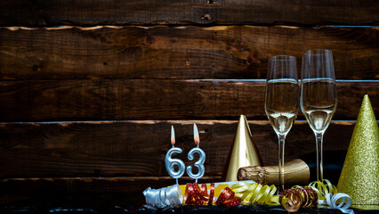 Solemn background for the anniversary with the number  63. Happy birthday background on brown wooden background with champagne bottle and champagne glasses. Beautiful holiday decorations copy space.