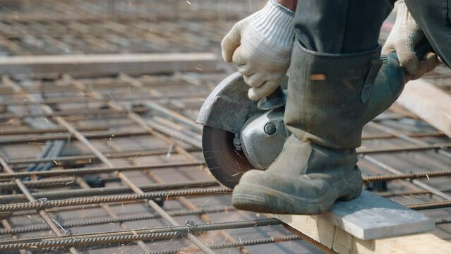 A builder cuts steel bars with a grinder to create the formwork of a construction site, sparks fly in slow motion
