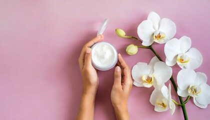 young woman moisturizes her hand with cosmetic cream lotion opened container with cream body milk white phalaenopsis orchid flowers on pink background flat lay top view minimalism style beauty concept