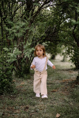 A small stylish girl, a child in beige trousers and a white blouse, runs in a tunnel from tall green bushes