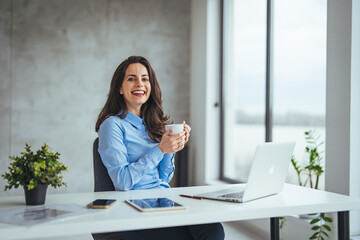 An attractive young businesswoman having coffee while working at her office desk. Laughing young ...