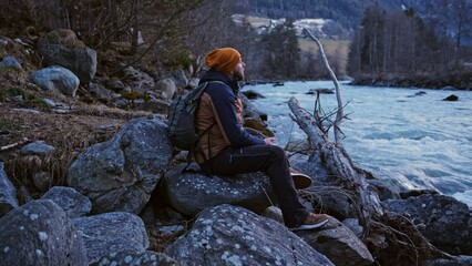 Caucasian Male Tourist Hiker Resting at Mountain River Bank on Cold Autumn Afternoon