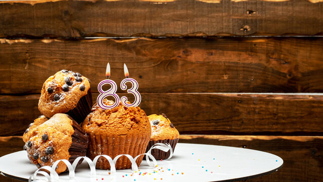 Pies with a number 83  of candles burning for the anniversary. Copy space background happy birthday on wooden background. Card or postcard festive rustic brown.