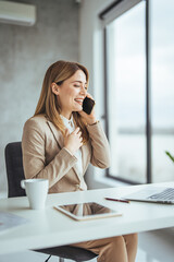 Happy freelancer using computer and talking on smart phone at office. Beautiful businesswoman working sitting at her desk in the office. 