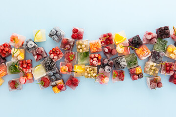 Blue background with ice cubes with frozen berries and fruits and mint