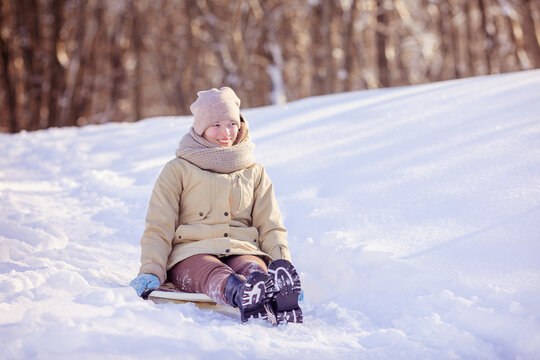 Happy teen girl in warm jacket and knitted hat and scarf riding down a snow slide in winter. Winter activities concept image. Happy family time. high quality photo. Copy space