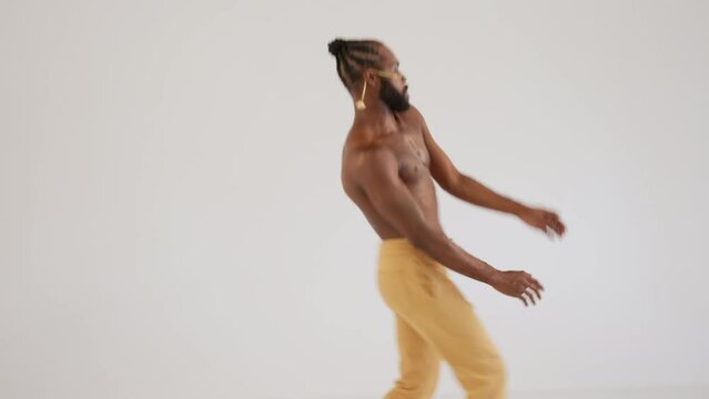 Young bearded African American gay man dancing with pride on white background. Shirtless male with bright makeup celebrating diversity and strength of personal charisma in studio.