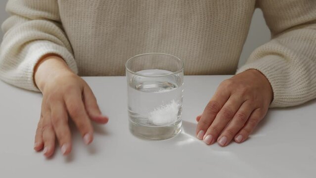 Woman sitting in front of glass of water with effervescent tablet, waiting for its total dissolving.
