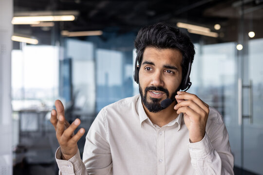 Close-up photo of a young Indian male businessman wearing a headset is in the office and talking and consulting through a microphone, gesturing with his hands