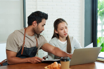 Obraz premium business couple owns small cafe Beautiful Asian girl stressed expression man many nationalities. Sitting laptop checking income offee shop, sales decreasing. bakery disposable brown paper coffee cups.