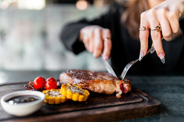woman hands with fork and knife eating beef steak in cafe