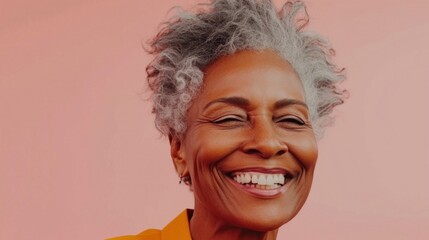 A joyful woman with gray hair smiling broadly showing her teeth against a soft pink background.