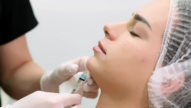 In a medical office, a cosmetologist gives beauty injections to a young woman’s chin. The concept of modern procedures in cosmetology.