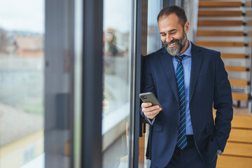 Smiling mature businessman holding a smartphone in an office. Businessman looking at the camera...