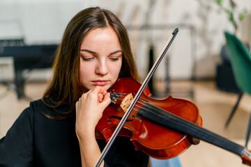 Close-up of a girl holding a violin picking strings with a bow to perform a classical music...