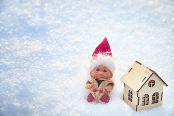 Cute little funny dwarf and small wooden house in snow in winter landscape. Wizard on a snowy background. Christmas and New Year