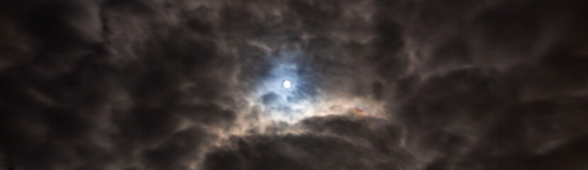 Fototapeta na wymiar moon glowing through the clouds at night with a strong thunderstorm front during rain