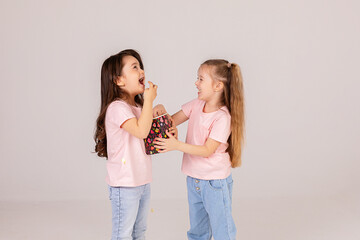 Two little girls holding a bucket of popcorn on a white background. Cinema and movie concept