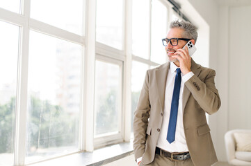 Senior businessman during a conversation on his phone, looks out window in a stance of thoughtful...