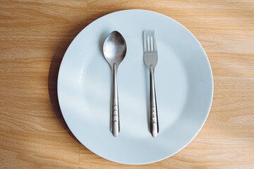 1 empty white plate and 1 pair of cutlery with a wooden background.