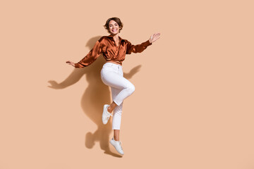Fototapeta na wymiar Full length photo of carefree shiny woman wear brown blouse jumping high empty space isolated beige color background