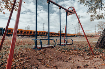 Fototapeta na wymiar empty swings on an empty playground without people against the background of burnt trains in Ukraine
