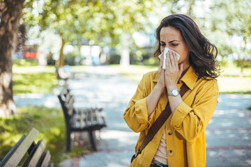 Woman with allergy symptom blowing nose. Outdoor shot of displeased Caucasian woman feels allergy,...