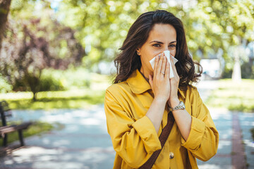 Woman Blowing Her Nose With Handkerchief In Public Parkf. Sick Young Woman With Seasonal Influenza Blowing Her Nose On A Tissue.  - obrazy, fototapety, plakaty