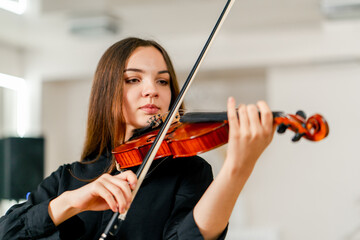 A young violinist plays with a bow on the strings of her violin against the background of musical instruments at the rehearsal base