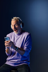 joyful surprised mature man with beard and headphones enjoying music and looking at his phone
