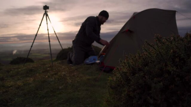 A wild camping photographer doing something beside a tent and camera tripod in shallow focus
