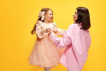 Birthday celebration. Stylish happy mother dancing with her little pretty daughter, kid against yellow studio background. Concept of happiness, Mother's day, childhood, fashion and lifestyle