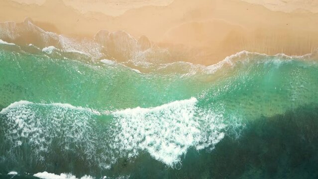 Aerial view of an empty sandy beach with slow moving beautiful waves on a sunny day.