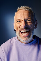 cheerful mature man with gray beard and casual trendy attire grimacing and looking at camera