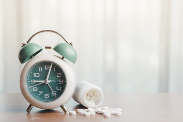 An alarm clock with a white plastic bottle containing medicine on the table for time management and healthcare concept