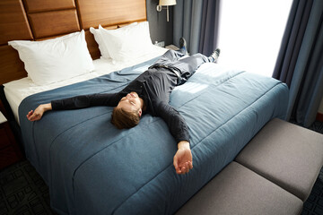 Guy lies with his arms outstretched on a large bed