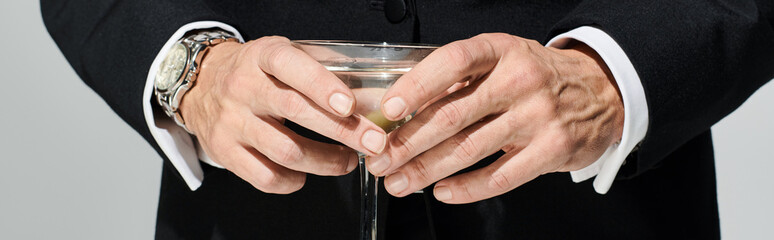 Obraz na płótnie Canvas cropped view of glass of delicious martini with green olives in it in hands of mature man, banner