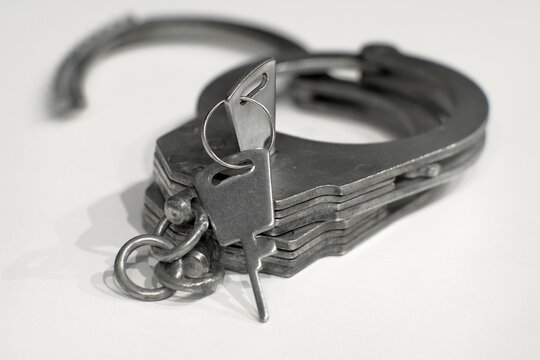 The image features a close-up shot of a handcuff partially open with its key attached, resting against a plain white backdrop