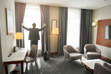 Man in travel clothes opens the curtains in hotel room