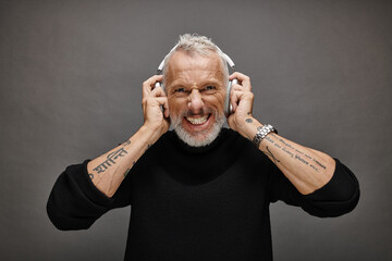 cheerful handsome mature man in stylish black turtleneck with modern headphones looking at camera