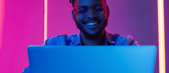 A man sits happily in front of his laptop, his eyes gleaming with a smile. The vibrant colors of purple, azure, and violet surround him as he enjoys the entertainment of magenta music.