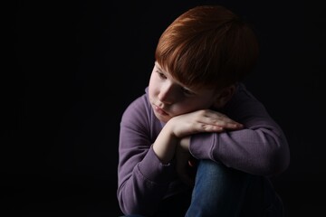 Portrait of sad little boy on black background, space for text