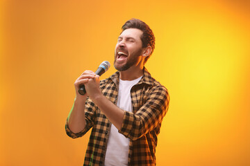 Handsome man with microphone singing on golden background