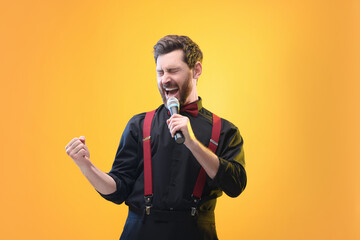 Emotional man with microphone singing on yellow background